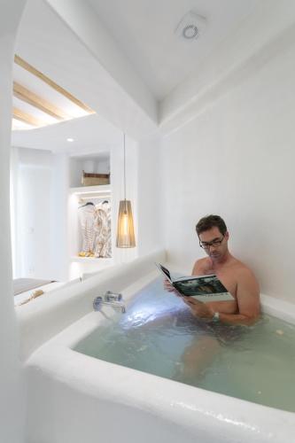 a man sitting in a bath tub reading a book at Majestique of Naxos luxury suites in Naxos Chora
