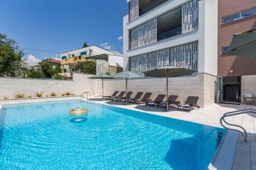 einem Pool mit Stühlen und einem Sonnenschirm neben einem Gebäude in der Unterkunft Abalone Apartments in Dramalj