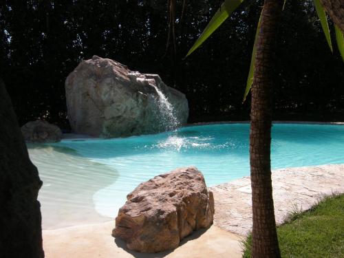 a rock in a swimming pool with a waterfall at Agriturismo Villa Gaia in Càbras