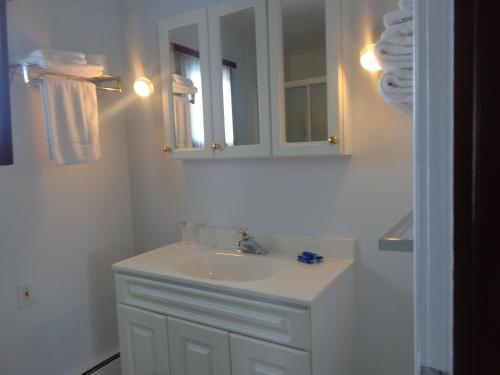 Baño blanco con lavabo y espejo en Happy Motel, en Edmundston