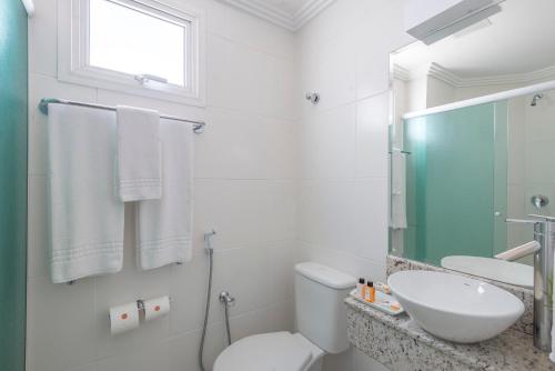 a white bathroom with a toilet and a sink at Hotel Glória Blumenau in Blumenau