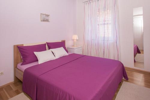 un letto viola in una camera bianca con finestra di Apartment Lavender a Vela Luka (Vallegrande)