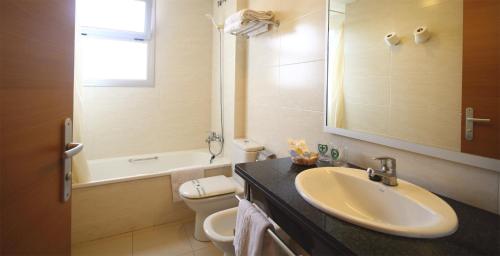 een badkamer met een wastafel, een toilet en een spiegel bij AQUA Hotel Nostre Mar Apartments in Pineda de Mar