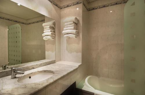 een badkamer met een wastafel, een bad en een spiegel bij Hotel Claude Bernard Saint-Germain in Parijs