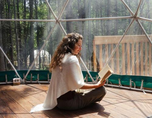a woman sitting on a deck reading a book at Centre de l'Hêtre in Lac-Beauport