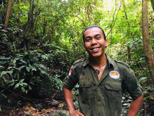 a man in a green shirt standing in a forest at Sahnan Guest House in Bukit Lawang