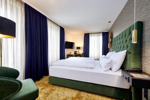 a bedroom with a large white bed and a green headboard at Das Carls Hotel in Düsseldorf