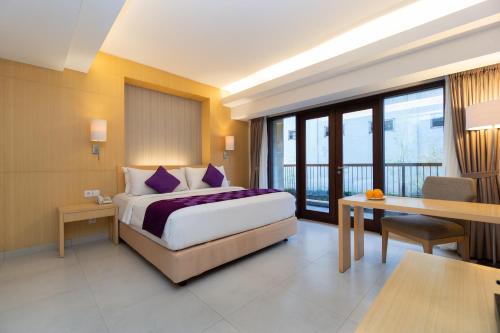 a hotel room with a bed and a table and a desk at Quest Hotel Kuta by ASTON in Kuta