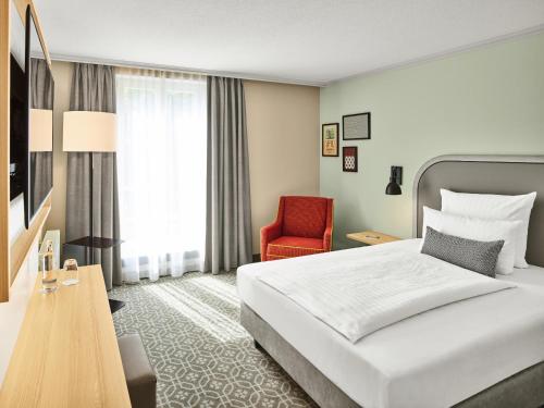 a hotel room with a bed and a red chair at MAXX Hotel Sanssouci Potsdam in Potsdam