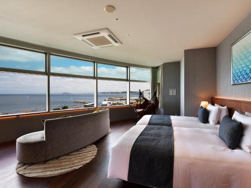 a hotel room with a bed and a chair and windows at Hayama Umino Hotel in Hayama