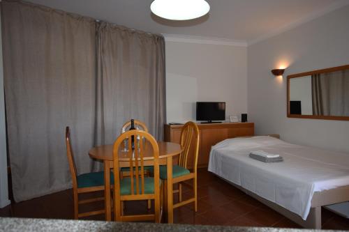 Cette chambre comprend une table, des chaises et un lit. dans l'établissement Lovely Estrela Vau Apt - Swimming pool view, à Portimão