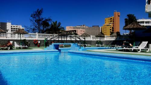 een groot blauw zwembad met gebouwen op de achtergrond bij Studio in perfect location in Playa de las Americas