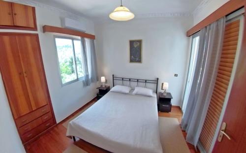 a bedroom with a bed with white sheets and two windows at Casa di Sole in Nikiana