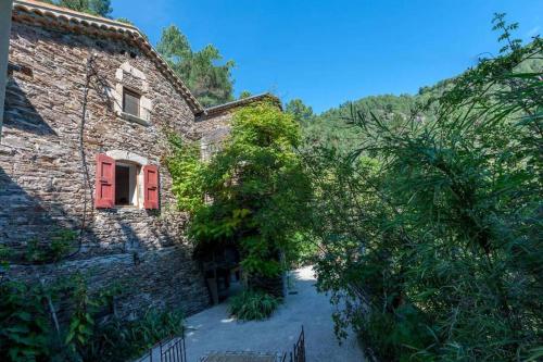 an old stone house with a red door and trees at Le mas des sources cevenol Le chambon in Le Chambon