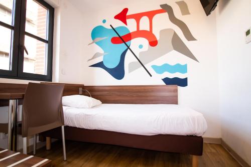 a bedroom with a bed and a table and a wall at Hôtel le Pastel in Toulouse