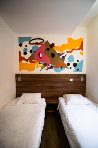 two beds in a room with a painting on the wall at Hôtel le Pastel in Toulouse