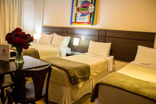 una camera d'albergo con due letti e un tavolo con un vaso di fiori di Hotel Maruá a São José dos Campos