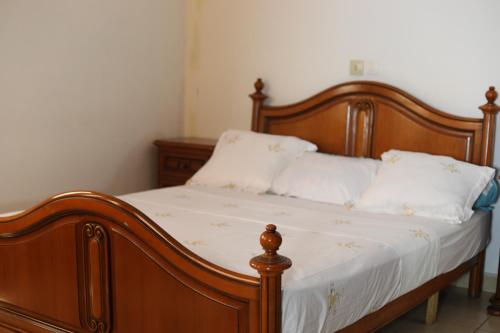 sypialnia z drewnianym łóżkiem z białą pościelą i poduszkami w obiekcie Appart TSINGA w mieście Mokolo