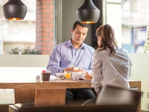 a man and a woman sitting at a table with a plate of food at Ibis Aéroport Bâle Mulhouse in Saint-Louis