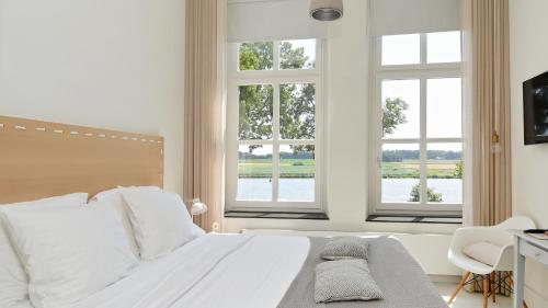 a bedroom with a white bed with two windows at Het Raadhuys - design B&B in Kessel