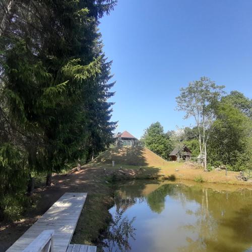 a river with a bridge and trees and a house at ŠMITI in (( Čūskumuiža ))