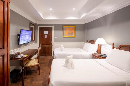 a hotel room with two beds and a desk and a television at The Orchid House 153 in Bangkok