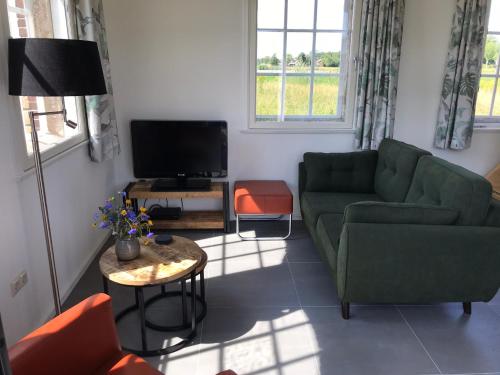 uma sala de estar com um sofá verde e uma televisão em Vakantiewoning Het Gemaal em Oostwold