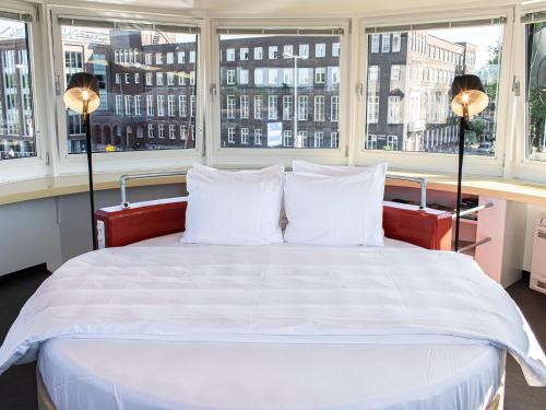 a bed with white sheets and pillows in a room with windows at SWEETS - Kortjewantsbrug in Amsterdam