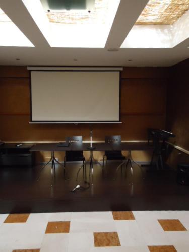 a projection screen in a room with chairs and a board at Tea Palace Hotel in Casapulla