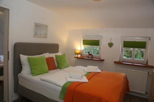 a bed with green and orange pillows and two windows at Hotel-Berggasthof Schwarzwaldperle in Sasbachwalden