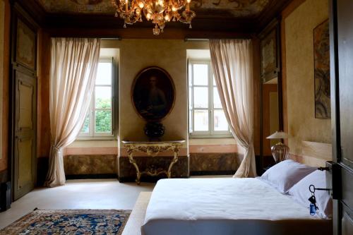 a bedroom with a bed and two windows and a chandelier at Antica Dimora Gallo Basteris in Piozzo