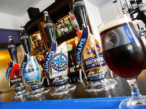 a glass of beer on a bar with beer bottles at Kings Head Hotel in North Elmham