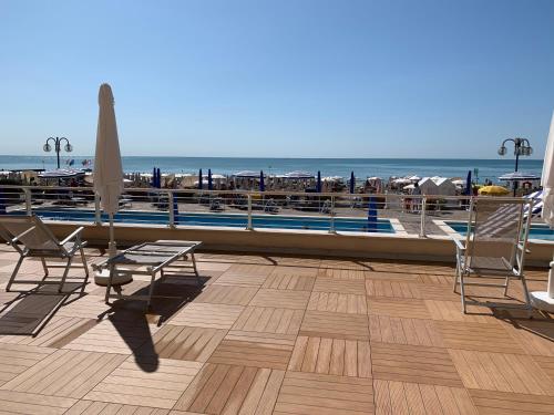 um deque com cadeiras, um guarda-sol e uma piscina em Sea view apartment with swimming pool em Lido di Jesolo