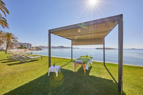 a pavilion with two chairs and a table on the grass by the ocean at Hotel Torre del Mar - Ibiza in Playa d'en Bossa
