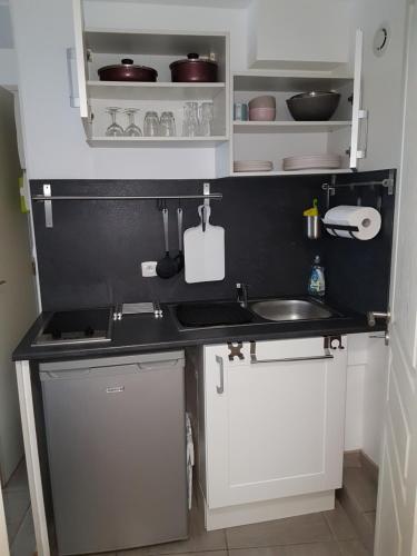 Elle comprend une petite cuisine avec un évier et des placards blancs. dans l'établissement Charmant studio au coeur de St Leu hyper centre, à Amiens