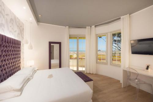 a white bedroom with a bed and a desk and windows at Park Hotel Pineta Boutique Hotel in Caorle