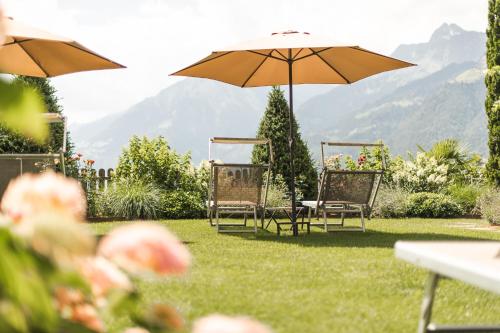 a group of chairs and an umbrella in the grass at Hotel - Appartements Schmied Hans in Schenna
