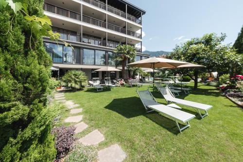 a group of lounge chairs and an umbrella in a yard at Hotel - Appartements Schmied Hans in Schenna