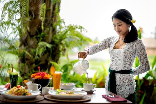 a woman pouring tea into a table with food at Cenik Villa Ubud in Ubud