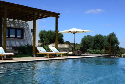 a swimming pool with lounge chairs and an umbrella at Vistas - Herdade do Zambujal in Castro Verde