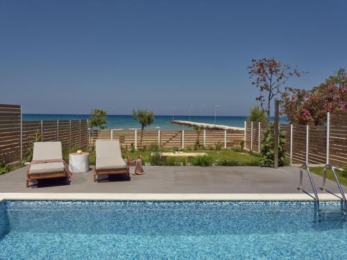 a swimming pool with two lounge chairs and the ocean at Maritimus Excelsior in Alykes