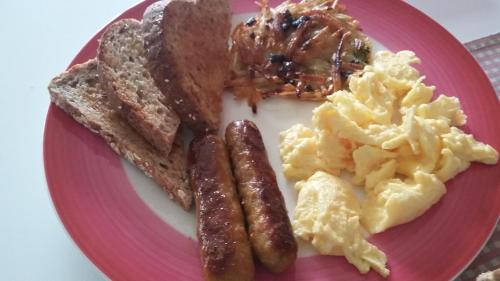 a pink plate of breakfast food with sausage and eggs at Vancouver Traveller B&B in Vancouver