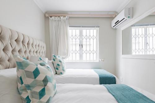 Banana palm luxury cottage في ديربان: سريرين في غرفة بيضاء مع نافذتين
