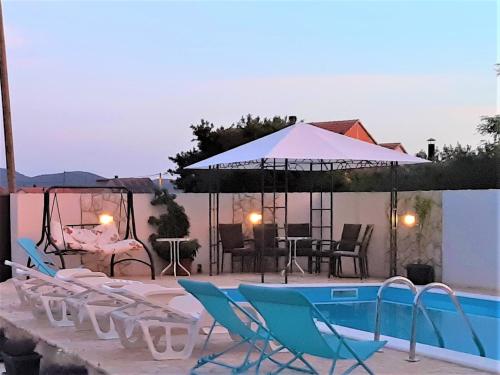 einen Pool mit Stühlen, einem Tisch und einem Sonnenschirm in der Unterkunft Apartments"Nika" with private pool in Galovac
