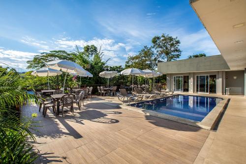 a patio with tables and chairs and a pool with umbrellas at Alegro Hotel in Jarinu