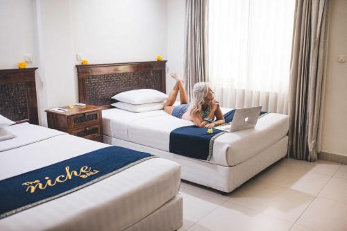 a woman laying on a bed in a hotel room with a laptop at The Niche Bali in Legian