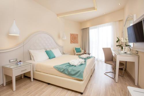 Schlafzimmer mit einem Bett, einem Schreibtisch und einem TV in der Unterkunft Pegasos Deluxe Beach Hotel in Faliraki