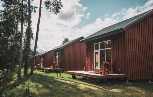 una casa roja con una terraza y sillas delante de ella en Atpūtas Bāze Ods LOFTS, en Bārta