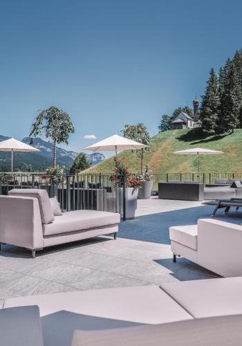 eine Terrasse mit weißen Sofas und Sonnenschirmen in der Unterkunft Das Kaiserblick 4 Sterne Superior in Ellmau