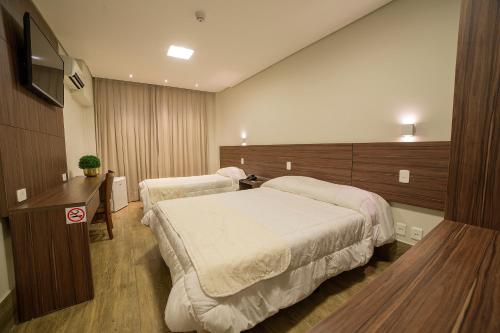 a bedroom with two beds and a desk and a television at Hotel Leiria in Matão